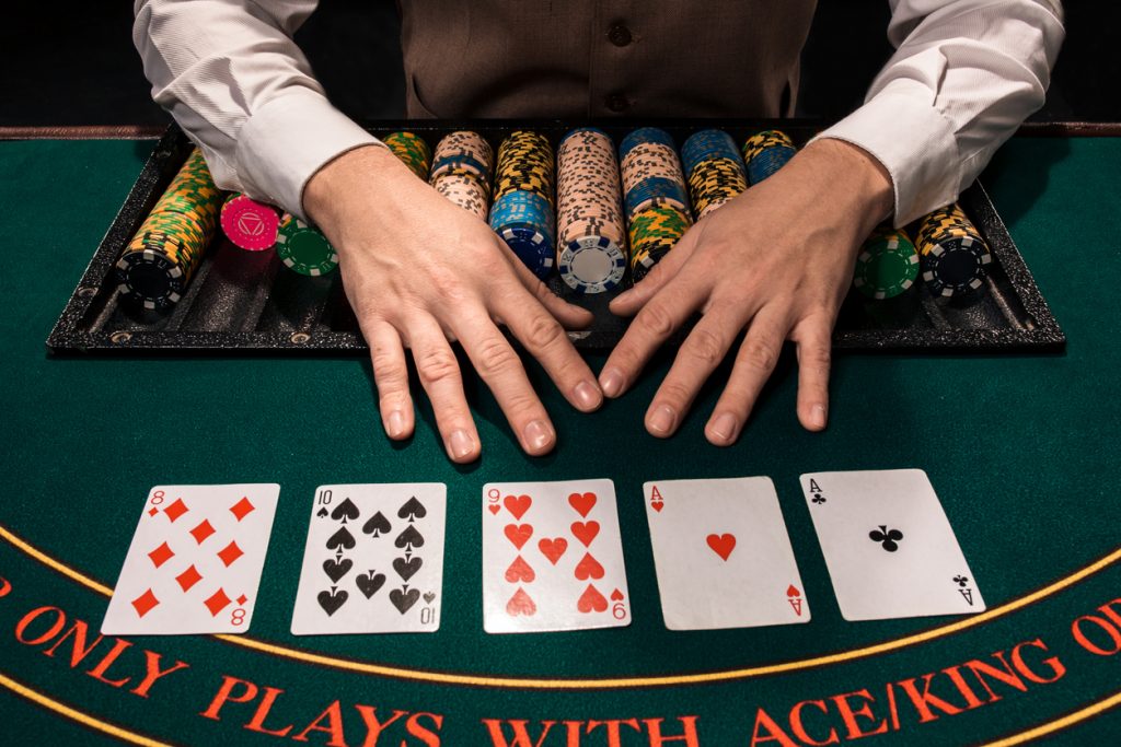 Casino, gambling, poker, people and entertainment concept - close up of holdem dealer with playing cards and chips on green table