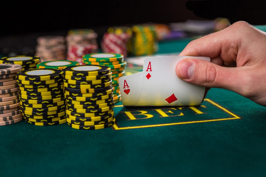 Close-up of male poker player lifting the corners of two cards aces at green casino table with aces